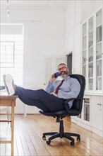 Caucasian man with feet up talking on cell phone