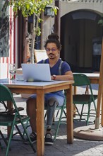 Mixed race man with prosthetic leg using laptop at sidewalk cafe