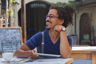 Smiling mixed race man using digital tablet at sidewalk cafe