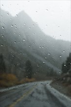 Mountains and rural road through wet window