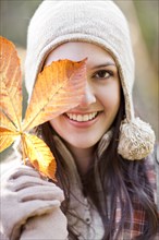 Mixed race woman in cap holding autumn leaf