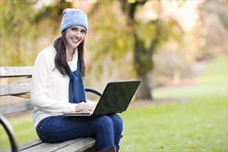 Mixed race woman in cap using laptop in park