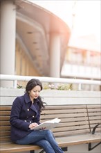 Mixed race woman sitting on bench reading