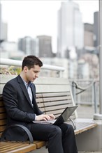 Mixed race businessman using laptop on city bench