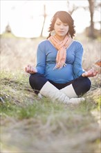 Pregnant mixed race woman practicing yoga in field