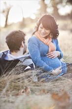 Pregnant woman sitting in field with husband