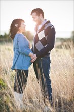 Pregnant woman holding husband's hands in field