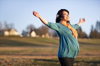Pregnant mixed race woman in field with arms outstretched