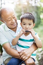 Chinese grandfather watching grandson with harmonica