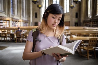 Chinese woman standing in library reading book
