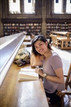 Smiling Chinese woman sitting in library reading book