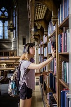 Chinese woman standing in library choosing book