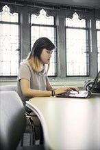 Chinese woman sitting in library using laptop