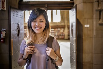 Chinese woman standing in library carrying backpack