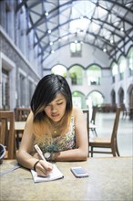 Chinese woman sitting in library writing in notebook
