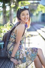 Portrait of smiling Chinese woman on bench wearing backpack