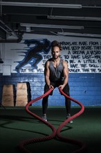 Mixed Race man lifting heavy ropes in gymnasium