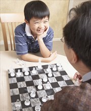Asian father and young son playing chess