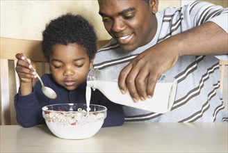 African American father pouring milk into young son's cereal