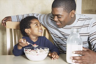Young African American boy eating cereal with father