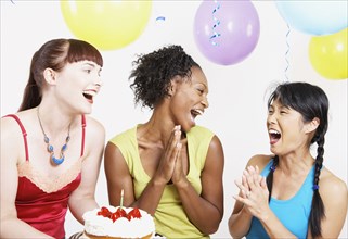 Three women laughing with cake at party