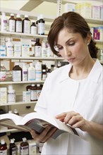 Female pharmacist looking at book in pharmacy