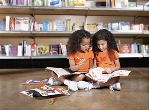 Two young sisters reading books in library