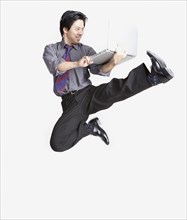 Studio shot of Asian businessman jumping in air with laptop