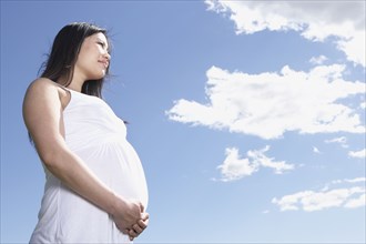 Low angle view of pregnant Asian woman under blue sky