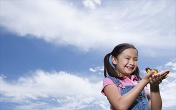 Young Asian girl holding butterfly outdoors
