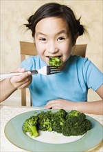 Young Asian girl eating broccoli