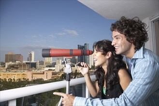 Hispanic couple looking through telescope on balcony
