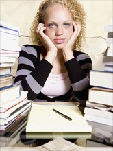 Young woman studying at desk with large stacks of books and notepad