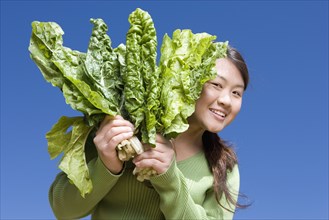 Asian woman holding bunch of green leaf vegetables