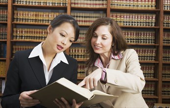 Multi-ethnic women looking at library reference book