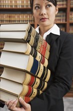 Asian woman carrying stack of library reference books