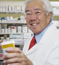 Senior Asian pharmacist holding medication bottle
