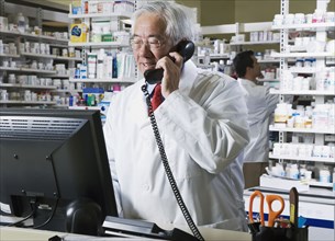 Senior Asian pharmacist talking on telephone