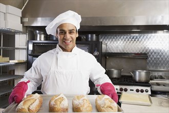 Hispanic male baker holding tray of fresh bread