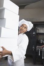 Mixed Race female pastry chef carrying stack of boxes