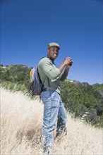 Mixed race man backpacking on hillside with binoculars