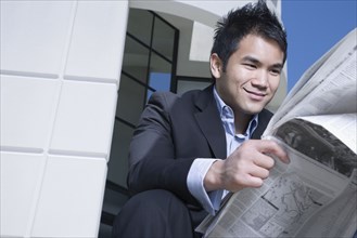 Asian businessman reading newspaper outdoors