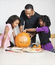 Father and daughters carving pumpkin