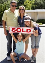 Excited Caucasian family holding "sold" sign
