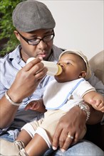 African American man feeding baby son bottle