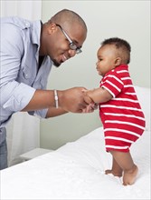 African American father helping baby son to stand up