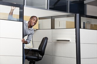 Mixed race businessman peering out from office cubicle