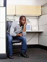 Serious mixed race man sitting in office cubicle