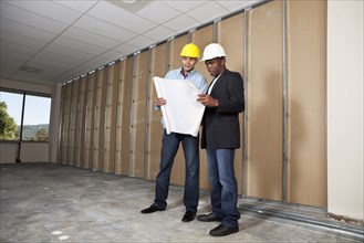 Mixed race businessmen looking at blueprints in room under construction