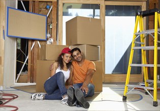 Hispanic couple sitting with cardboard boxes in new house